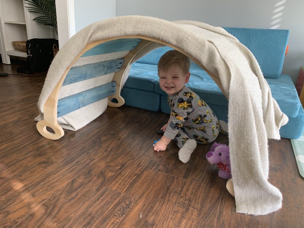 pikler climbing arch with a blanket on top to make a cave