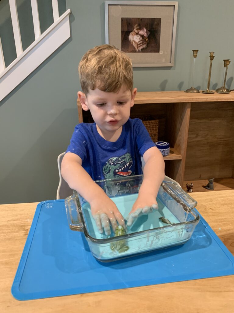 toddler playing with frog life cycle sensory bin with blue oobleck