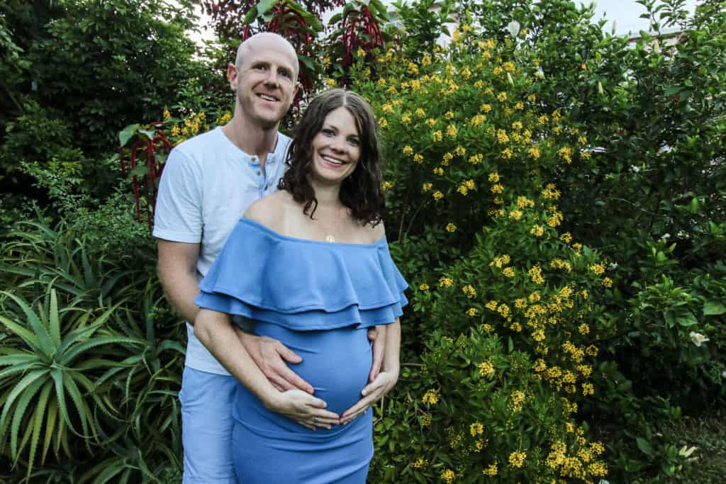 couples maternity photo in front of greenery