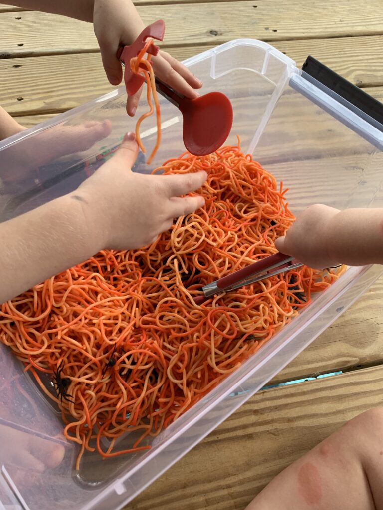 sensory bin with orange spaghetti and black plastic spiders