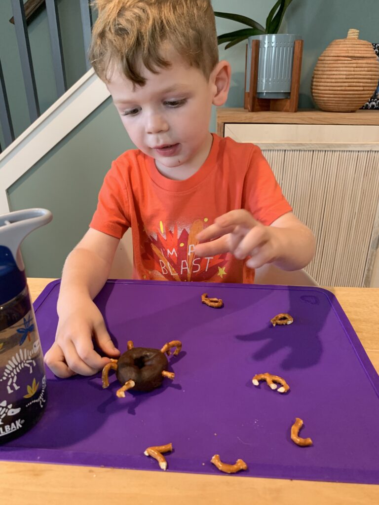 toddler adding pretzel legs to spider donuts
