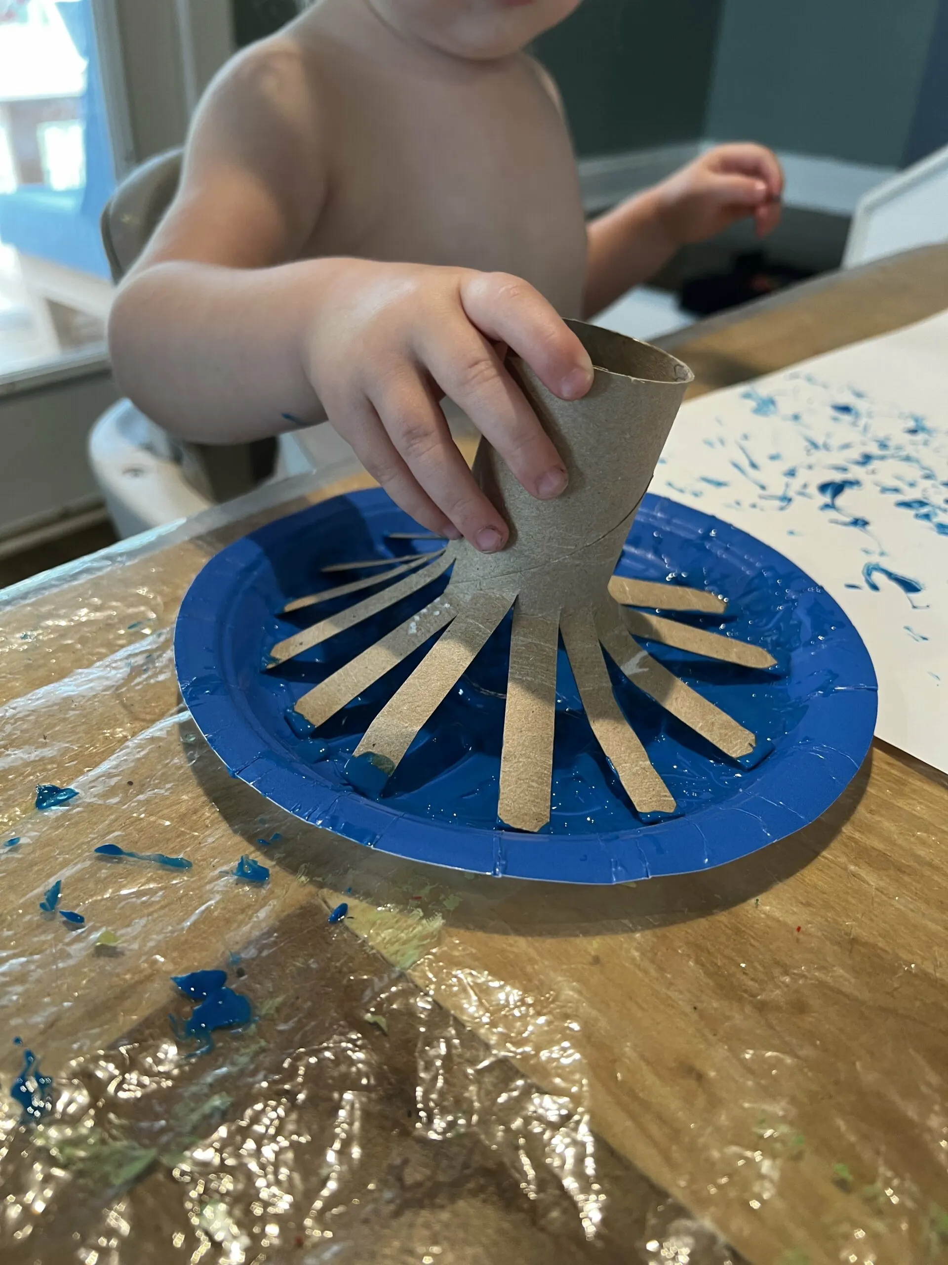 toddler dipping cardboard tube into paint
