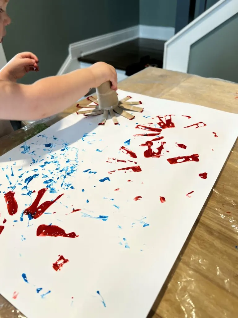 toddler painting fireworks with a toilet paper roll
