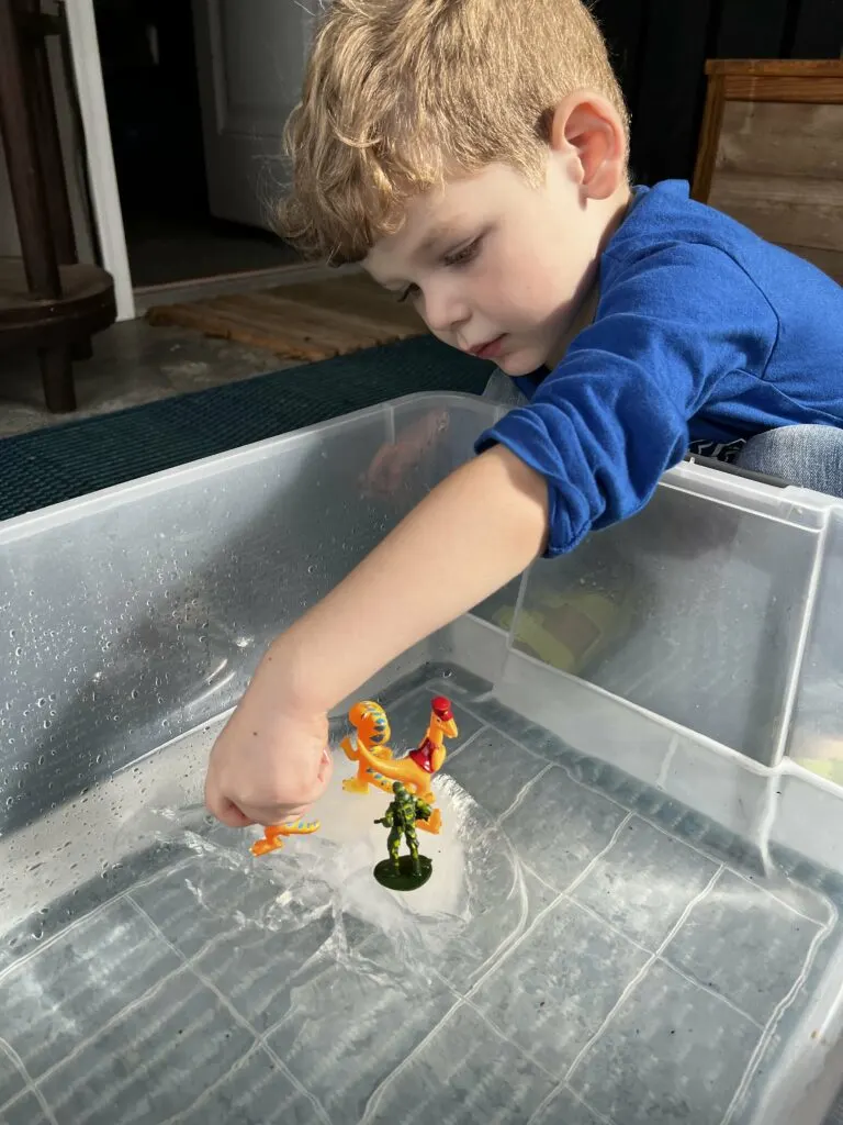 toddler playing with ice in water sensory bin