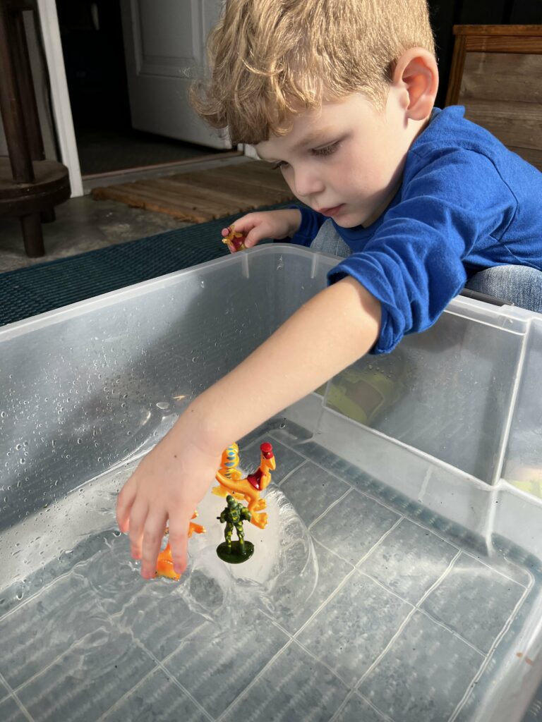preschooler playing with ice in water sensory bin