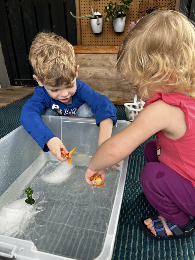 toddler playing with ice in water sensory bin