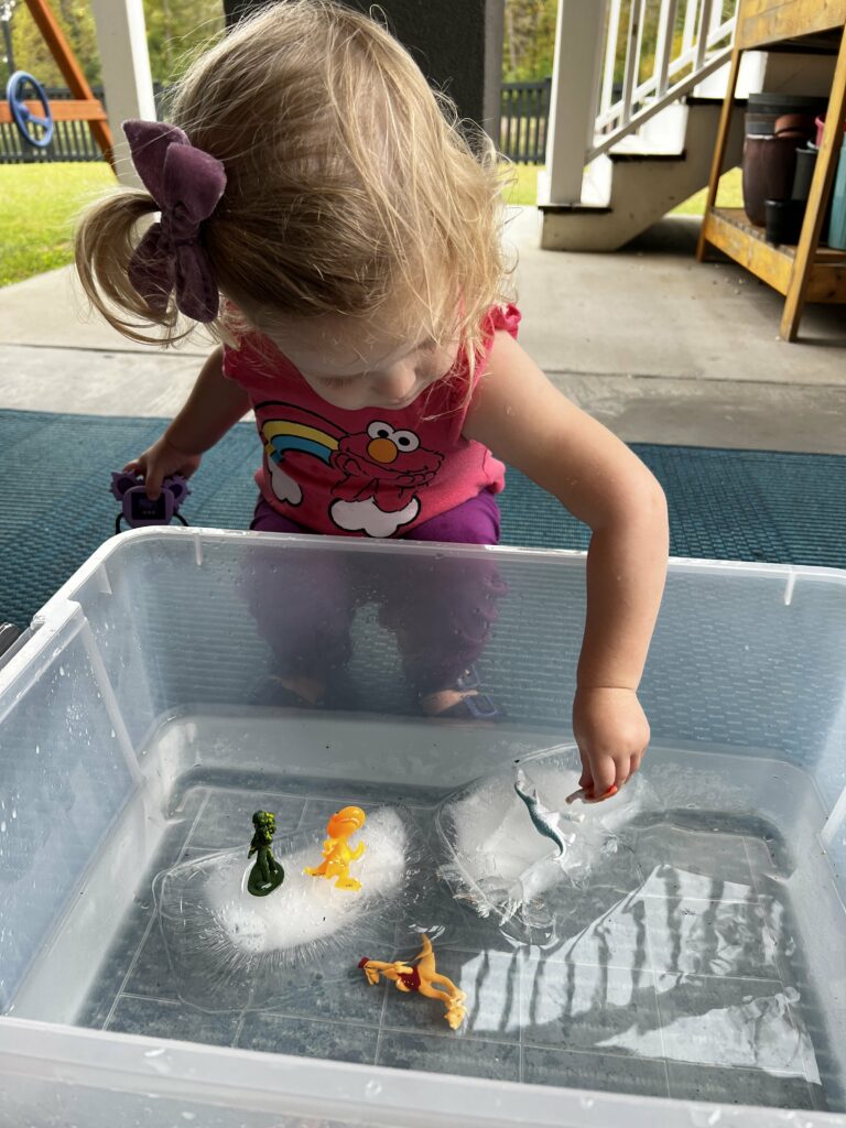 toddler playing with ice in water sensory bin