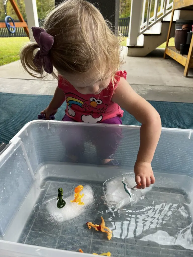 toddler playing with ice in water sensory bin