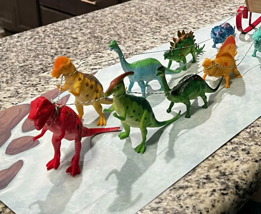 elf on the shelf in a sleigh with dinosaurs pulling it