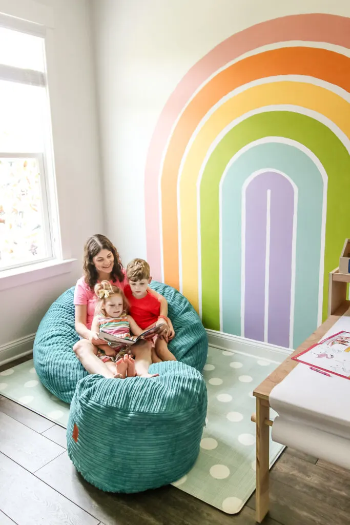 reading to kids in bean bag chair in front of rainbow mural