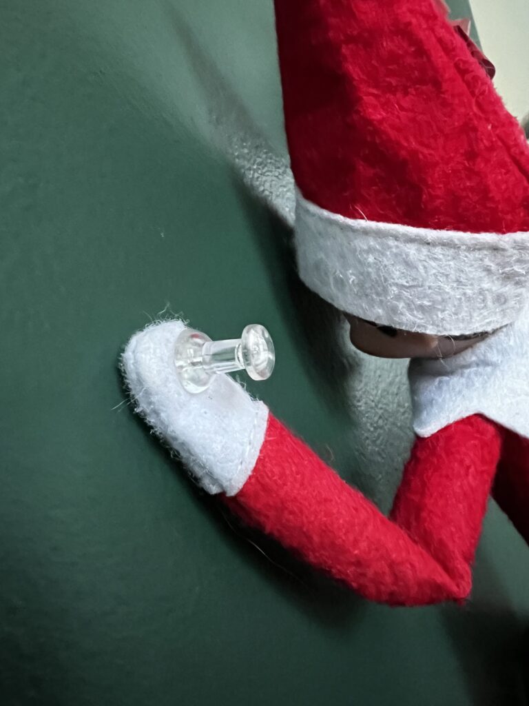 elf on the shelf thumbtacked to wall