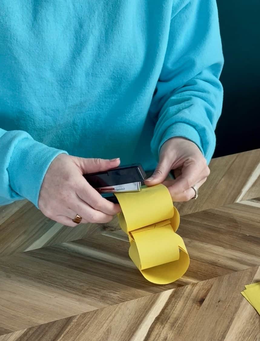 stapling yellow paper strips into a rapunzel paper chain